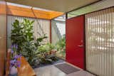 The entryway of the home is characterized not only by the red front door, but also by the large panels of glass on either side, including one that almost disappears, allowing the planting box to appear to continue seamlessly into the interior.
