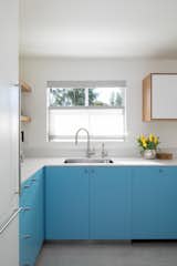 Kitchen, White Cabinet, Colorful Cabinet, and Engineered Quartz Counter Having the sink in front of the window is a classic feature in many homes, and here it allows for views out to the well-used pool.  Photos from Budget Breakdown: An Interior Designer Livens Up Her Dated Kitchen for $57K