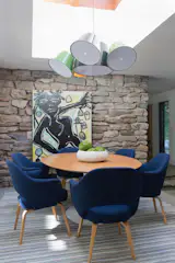 The dining area is raised up from the rest of the living space, reached by a few steps covered in fieldstone. Bold color choices for the light fixtures and chairs create a contrast with the stone walls and floor.