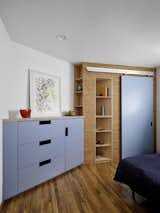 The former office is transformed into a bedroom with new storage that resolves the awkward angle in the room. The wall of custom cabinetry includes a chest of drawers, closets, and shoe racks.