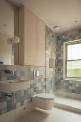 Shades of calming blue tile line the bathroom walls, paired with plywood cabinetry treated with linseed oil.