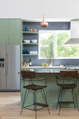 For the kitchen, the architect selected a recycled Fireclay Tile in Slate Blue and paired that with High Park paint from Benjamin Moore. Copper pendants from VITA accent the space. The vent hood is mounted in front of a large window, bringing in natural light and allowing for a view of the herb garden.