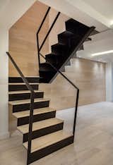 A wood backdrop soars up the back of the stair. The railings kiss the wall and disappear.