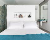 The white wall behind the bed divides the bath area from the bed area. The turquoise blue tiles on the shower and the basin were designed and produced by Maria Ulecia on her atelier and create the colour scheme for the bedroom