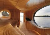 The sinuous interior is lined with CNC-cut wooden panels that define stepped sauna seating and porthole windows.
