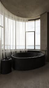 Soft natural light highlights the textured concrete walls and the smooth black bathtub overlooking the sea. 

#EO3H #sirotovarchitects #minimalism