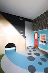 In a home in Los Angeles, a child's bedroom has been outfitted with custom carpeting and millwork, a reading nook under a staircase, a mini door and window, and a magnetic chalkboard wall.