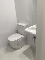 A simple  minimalist bathroom; toilet, sink with mirror, and shower opposite.