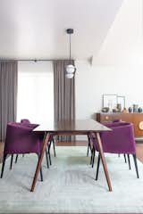 A bold, refined color palette. The dining room combines mid-century magenta-colored chairs with tailored wooden pieces. Neutral window treatments tie the space together, adding an understated elegance. 