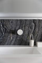For a cohesive look, marble is used as the sink backsplash and pulled out along the bathroom wall with the multi-hued black, grey, bronze and white veining, juxtaposed against crisp white detailing and natural wood elements. 
