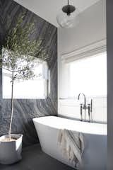 To create a rejuvenating space, the freestanding tub is nestled in the sun-drenched corner. Marble on one wall. White paint on the other. 