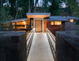 Bridge Entry | To enter the home, guests arrive on an upper bluff and cross a foot bridge to the front door. The bridge draws immediate attention to the home’s signature folded roof plane, which appears to hang effortlessly in the shadow of a deep canopy of cottonwood trees. 