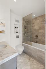 In the bathroom, the homeowner chose to continue the marble theme with herringbone floors, a warm subway tile on the walls, and the same 2-inch-thick Carrara marble from the kitchen as a counter. With a frameless glass divider, the deep soaking tub does double duty for baths and showers. Three well-placed niches, including one inside the tub area, add storage for toiletries and small décor objects.