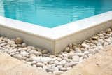 Ivory Travertine was used for the pathway and decking around the pool White-Iced tile surrounds the infinity edge. White river rock is used in keeping with the same color palette. It not only serves as a design element but also hides the grate surrounding the pool for the over-spill.