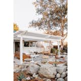 Outdoor, Side Yard, Desert, Boulders, Trees, Concrete, and Shrubs This pergola-covered seating area, complete with hanging chairs, is off the living room.  Outdoor Side Yard Concrete Desert Shrubs Photos from A Chic, Renovated A-Frame in Palm Springs Asks $535K