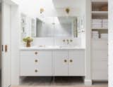 A Carrara marble counter and backsplash, concrete floors, a frameless mirror, and white cabinets keep the look seamless and consistent in the bathroom. 