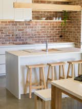Kitchen, Cooktops, White Cabinet, Concrete Floor, Pendant Lighting, Drop In Sink, and Brick Backsplashe The kitchen stools are from Tuscan Outdoor Tables, a Dandenong, Victoria outfit that crafts furniture from local Cypress and reclaimed timber.  Photos from A New, Affordable Green Home Comes to an Australian Eco-Village