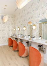 In the beauty room, floral wallpaper from Caitlin McGauley picks up the tangerine color of the chairs from Douglas &amp; Bec. Wall light sculptures from Cedar &amp; Moss illuminate the mirrors. 