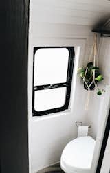 The bathroom hosts a composting toilet from Nature's Head and is spruced up with white wall paneling and a black-framed window. 
