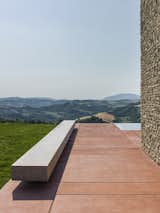 The rectilinear form of a floating concrete bench sits atop the red concrete pad that defines the exterior courtyard.