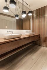 In the master bathroom, the teak vanity and wood screens were designed by Isaac-Rae and custom built by a furniture maker. The sinks by Apaiser were also made custom. The lighting is by Flos.

