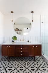 In a bathroom, a credenza found on Etsy was topped with marble and converted to a vanity. Tulum tile from the Cement Tile Shop covers the floors while elongated subway tile, laid in a vertical grid, updates the walls. Schoolhouse Electric pendants complete the look.