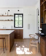 A modern desk was incorporated into the built-in walnut unit that separates the kitchen from the dining room, and has been accented with a Hans J. Wegner Wishbone Chair. The refrigerator and freezer columns are Thermador and the wall sconces are by Cedar &amp; Moss.
