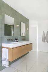After: In a Jack and Jill bathroom, a custom vanity topped with marble floats against a wall clad in Fireclay tile. The mirrors are by Wayfair and the sconces are from Allied Maker.&nbsp;Samuel designed the unique brass inlay pattern for the terrazzo floors.