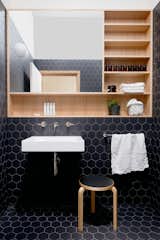The powder room is a retreat from the main living areas. The firm set off the Victorian ash storage and mirror unit by surrounding it with black hexagon tile. A "sky tunnel" in the ceiling floods the room with natural light. 