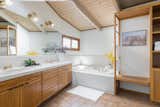 The master bathroom has a simple tile treatment and wood storage units.