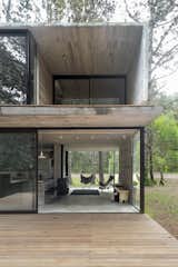 Luciano Kruk perforates a concrete volume with glass walls to fashion a simple yet elegant vacation home in the province of Buenos Aires. On a quiet lot populated with aged pinewood, Luciano Kruk designed a modest vacation home for three sisters and their families. The 807-square-foot, two-level home is ensconced in its forest setting. The firm employed board-formed concrete inside and out to connect the building with its environment. "Pine planks were used to set the formwork so that the partitions, as well as the slabs, would preserve the texture of the wood veins in an attempt to establish a harmonious dialogue with the bark of the local trees," said the firm.&nbsp;