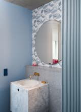 A petite floating marble vanity hugs a terrazzo wall. The wallpaper is the The Great Wave by Cole & Son.
