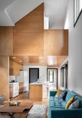 Standing three stories high, the 1,650-square-foot home hosts two bedrooms, two-and-a-half baths, and a bonus office.  Double-height ceilings increase the sense of space in the living room. Maple plywood wraps the kitchen cabinets and ceiling, as well as the accent wall.