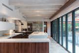 The kitchen and dining areas now occupy the new single-level wing and also overlook the backyard via the glass wall. Silestone countertops waterfall over walnut cabinetry, and exposed wood rafters overhead received a coat of whitewash.