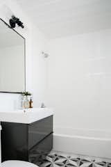 "We updated each of the guest bedrooms and full guest bathroom with whimsical tile and statement finishes," says the firm. The designers used a graphic patterned Merola tile on the floor, pairing it with a black vanity from IKEA and a CB2 Infinity Mirror. The light fixture is the Trent Austin Alguno 2-Light Vanity Light.