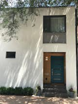 The concrete block is now covered in light-colored stucco, grey lap siding, and charcoal metal trim. The front door is painted teal and surrounded by clear-coated Maple.