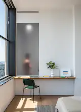 In a bedroom suite, a frosted glass panel allows light to flow into the adjoining bathroom’s shower.