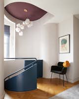 The design team subtly sculpted the wall around the top of the staircase. A CB2 Azalea Gray Mink chair sits in the hall.