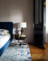 In the adjoining sleeping area, a one-of-a-kind rug woven from recycled sari silk, sourced from ABC Carpet, lies beneath a Hartley Bed from Room & Board in indigo velvet. The Pablo Lamp by Arteriors rests atop a steel-and-black-glass end table by Caligaris.