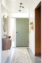 The firm swapped the door orientation and painted it sage green. They also preserved the surrounding lites to keep the natural light flowing inside. The original wall paneling on the right was painted a bright white, and new hooks corral coats.