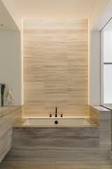The tub backdrop is composed of bamboo-cut textured marble tile. “When the lights are on, it casts a really beautiful waterfall effect of light across the texture,” says Watts.