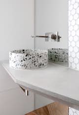 In a powder room at a luminous home in Australia, a terrazzo basin in the powder room makes a statement set atop a concrete countertop. Large-scale white penny tile continue the light color palette.