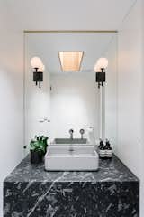 In the guest bathroom, another new skylight is wrapped in white oak. The counter is Fossil Black Stone and the sconces are Allied Maker.