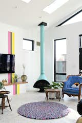 An aqua Malm fireplace warms up a corner. The pink, green, and yellow stripes now reach the skylights and extend over an integrated storage space to the floor. “My husband and I, we both actually hate having a TV visible to guests, but it’s a necessary evil,” says Shawn. “So how do you make that interesting and without it being too busy? [The rainbow stripe] creates an element that draws your eye away.”