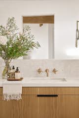 A terrazzo tile backsplash provides a lightly textured backdrop for the brass faucet and warm wood cabinetry.