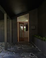 Now, a new flagstone walkway borders the preserved planter running alongside the wall. A custom pivot door with the semi-circular oak knob foreshadows the circular cut-out on the wall inside, and Berg added a quadrilateral-shaped window above the door that accentuates the ceiling angle.