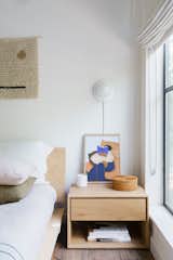 In the guest room, an Ethnicraft bedside table sits beside a Floyd bed. The wall sconce is from Human Home and the art from Poster Club. Shop Territory wall hangings add texture, and roman shades from the Shade Store envelope the windows.