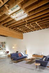 The newly exposed wood ceiling was walnut blasted to clean it up. “We knew that we would be looking up at it, looking up at the skylights, and watching the rainfall in the winter,” says Anna. “So, it would be nice to have it be a really warm and rich color, and to have it feel clean and tidy after so many years of just being a serviceable ceiling.” In the living room, two Raleigh sofas from Design Within Reach face each other.