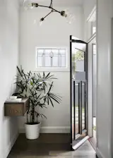 Engineered oak flooring in a darker stain covers the floors throughout. A Snelling studio Y-04 chandelier is a modern contrast to the new stained glass window, and a wall-mounted entry shelf with a drawer saves floor space.