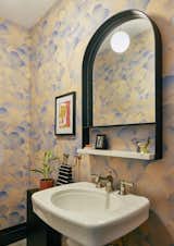 In a new powder room, the arch mirror with marble shelf is from CB2 and the wallpaper is Finisterra Azurite from Flat Vernacular.